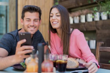 Restoranın terasında bir akıllı telefon ile mutlu genç çift oturma grubu