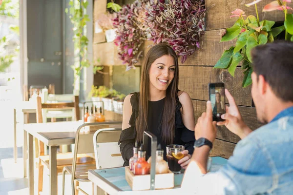 Happy young couple seating in a restaurant with a smartphone taking a photo