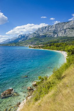 Adriyatik Denizi Hırvatistan Avrupa. Mavi gökyüzü ve okyanus güzel renkli güneşli yaz günü. Dağlar, bulutlar, rock ve resif. Güzel temiz su. Plaj ve yeşil ağaçlar. Mutlu ve rahatlatıcı bir atmosfer.