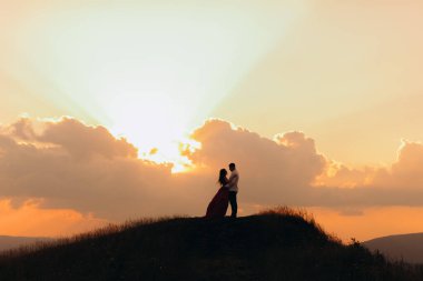 Gün batımında aşık olan genç bir çiftin silueti, öpüşür ve birbirlerine şefkatle bakarlar. Ağır çekim. Gün batımında genç bir çift.