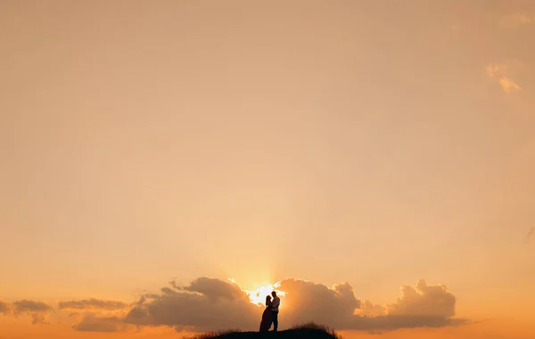 Σιλουέτα του νεαρού ερωτευμένου ζευγαριού που απολαμβάνει ένα ηλιοβασίλεμα πάνω από τα βουνά. Κορίτσι με κόκκινο φόρεμα. Καταπληκτική θέα των νέων αξιολάτρευτο ζευγάρι φιλιούνται στο πράσινο πυκνό βουνό — Φωτογραφία Αρχείου