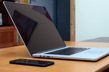 Oturma odasındaki ofis ortamında bir masada dizüstü bilgisayar ve akıllı telefondan görüntüle.