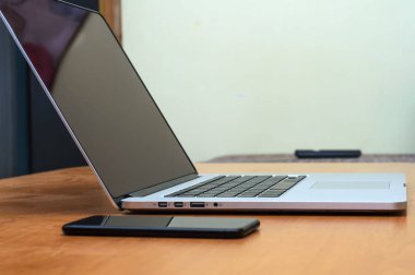 Oturma odasındaki ofis ortamında bir masada dizüstü bilgisayar ve akıllı telefondan görüntüle.