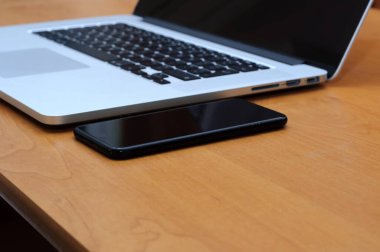 Oturma odasındaki ofis ortamında bir masada dizüstü bilgisayar ve akıllı telefondan görüntüle.
