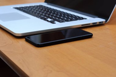 Oturma odasındaki ofis ortamında bir masada dizüstü bilgisayar ve akıllı telefondan görüntüle.