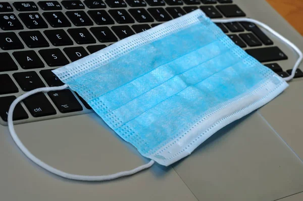 View on a medical mask protection against flu and other diseases like coronavirus on an open laptop pc.