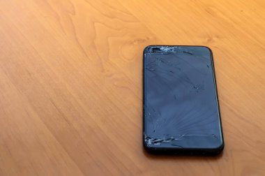 Kırık bir ekranda, ofis ortamındaki bir masanın üzerindeki akıllı telefonun görüntüsünü göster.
