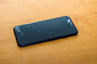 Kırık bir ekranda, ofis ortamındaki bir masanın üzerindeki akıllı telefonun görüntüsünü göster.