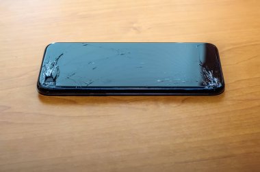 Kırık bir ekranda, ofis ortamındaki bir masanın üzerindeki akıllı telefonun görüntüsünü göster.