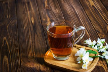 Bir fincan çay ile kahverengi ahşap zemin üzerinde Yasemin çiçekleri