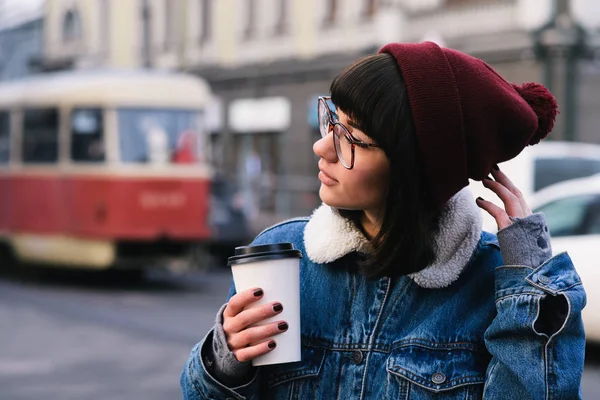 Stylish young hipster girl walks in the city and drinking coffee and straightens hair — Stock Photo, Image