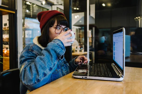 Portré egy lány csípő, aki használ egy laptop, és kávét iszik egy szép kávézó — Stock Fotó