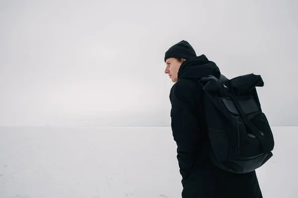 Indietro giovane uomo con uno zaino nero, viaggiando su luoghi invernali innevati — Foto Stock