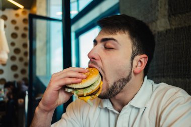 restoranda hamburger yeme ve tadı zevk sakallı genç bir adam