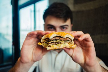 young man holding a delicious hamburhen and it is going to eat clipart