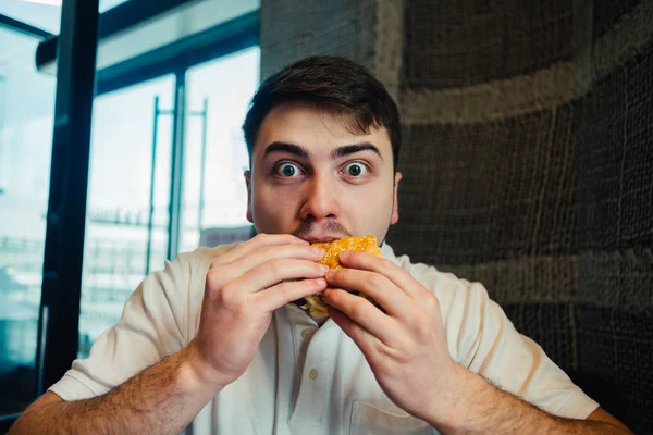 Молодой человек ест бургер в ресторане, и удивил свой необыкновенный вкус — стоковое фото