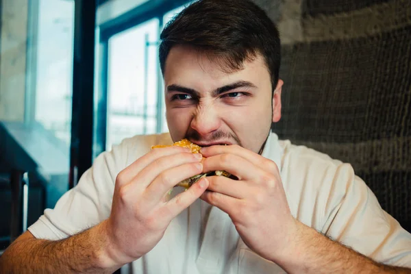 Young man eagerly eats burger — Stock Photo, Image