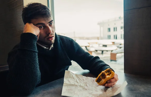 Um jovem com barba, sentado em um restaurante e não pode mais comer seu hambúrguer — Fotografia de Stock