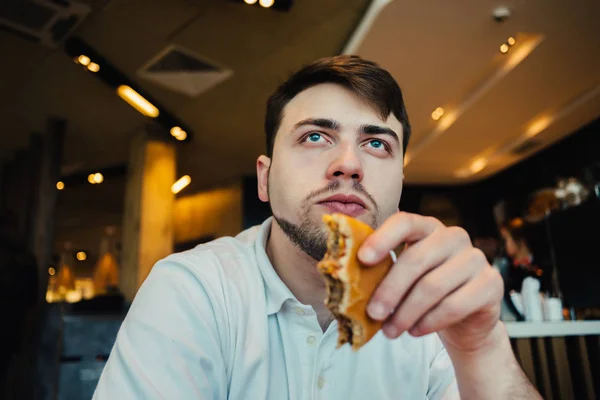 Een jonge man zitten in een leuk restaurant fastfood hamburgers en ontbijt — Stockfoto