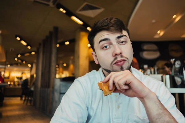 Een jonge man zitten in een leuk restaurant fastfood hamburgers en ontbijt — Stockfoto