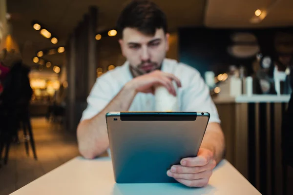 Joven hombre de negocios utiliza un Tablet PC en un acogedor restaurante en anticipación de su pedido — Foto de Stock