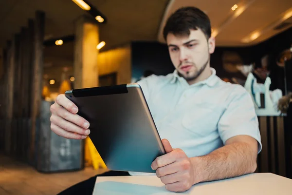 Un joven con barba sentado en el acogedor restaurante utiliza una Tablet PC —  Fotos de Stock