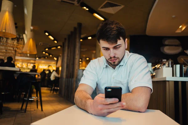 Un joven con barba disfruta del teléfono en un acogedor restaurante — Foto de Stock