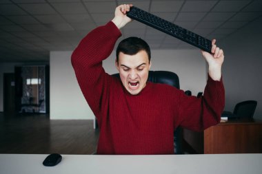 Yaklaşık senin klavye parçalamak için kızgın ofis çalışanı. Ofis durumda. Genç bir adam onun elinde bir klavye ile