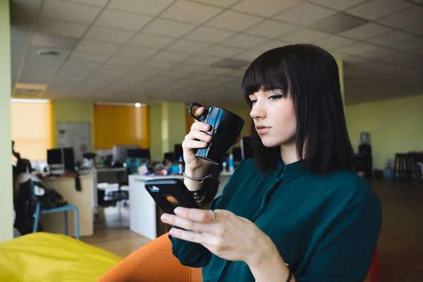 Siyah kahve içer ve bir cep telefonu kullanan bir genç, güzel bir kadın memur portresi. İş yerinde kırmak — Stok fotoğraf