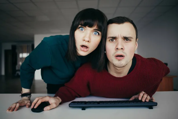 Young beautiful people puzzled look in the computer monitor. Emotional look at the camera — Stock Photo, Image