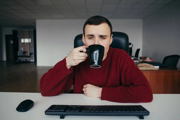 Retrato de un joven trabajador de oficina cansado tomando café en el trabajo. La situación en la oficina — Foto de Stock