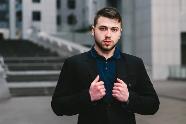 Retrato de un hombre serio hombre de negocios corrige ese traje en el fondo del paisaje urbano . — Foto de Stock