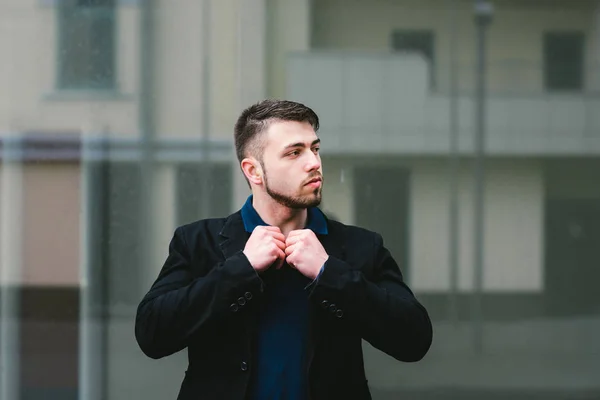 Retrato de um homem sério que corrige sua camisa e olha para um fundo cinza . — Fotografia de Stock