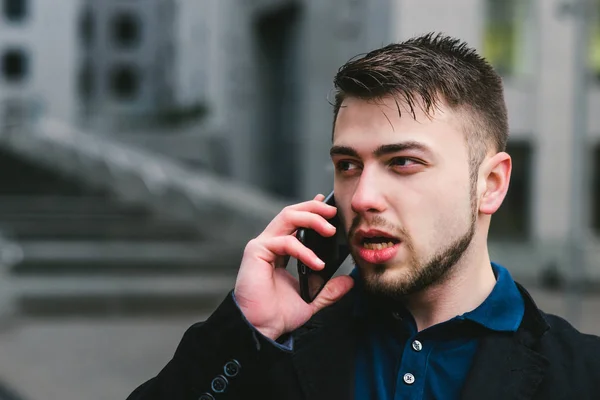 Retrato de joven hombre de negocios hermoso y serio hablando por teléfono en el contexto de la arquitectura moderna — Foto de Stock