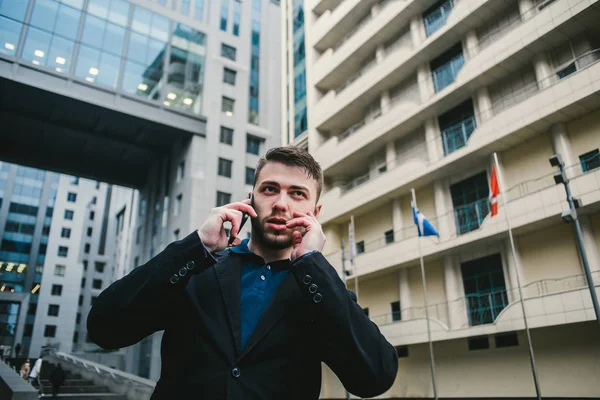 Um jovem homem com um empresário barba falando ao telefone no fundo de um moderno centro de negócios . — Fotografia de Stock