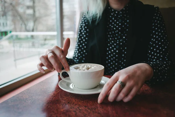 Rukou dívky si šálek kávy s marshmallows v útulné kavárně. Horký nápoj k snídani — Stock fotografie