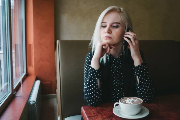 Jovem mulher de negócios falando ao telefone e beber café com marshmallows em um café acolhedor. Notificação . — Fotografia de Stock