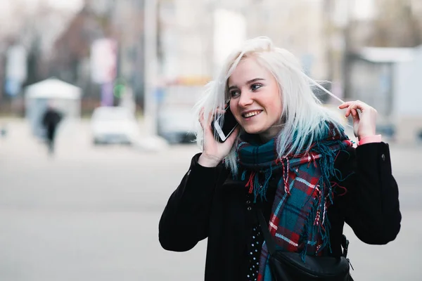 Εξωτερική πορτρέτο του ένα όμορφο θετική κορίτσι μιλάει στο τηλέφωνο. Η γυναίκα που χαμογελάει και ισιώνει τα ξανθά μαλλιά στο δρόμο — Φωτογραφία Αρχείου