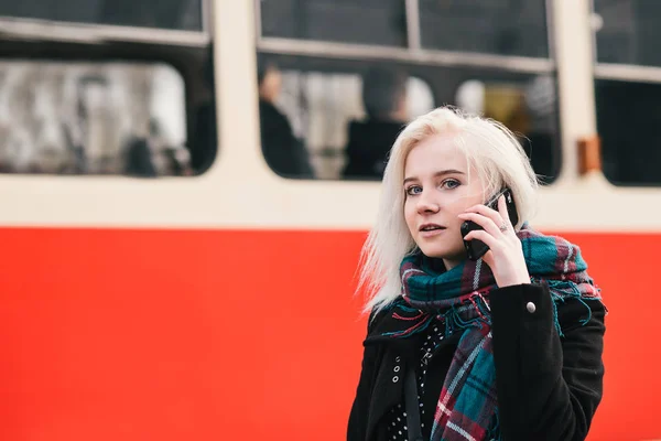 Νέοι όμορφη ξανθιά γυναίκα που μιλάει στο τηλέφωνο σε φόντο κόκκινο σιδηροδρομικό σταθμό. Εξωτερική πορτρέτο του ένα κορίτσι. — Φωτογραφία Αρχείου