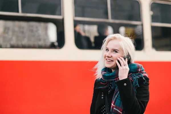 Młoda Blondynka dziewczyna uśmiechający się rozmawia przez telefon na tle czerwony pociąg. Zewnątrz portret dziewczynki. — Zdjęcie stockowe