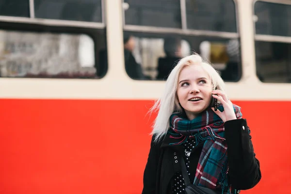 Młody uśmiechający się blond kobieta rozmawia przez telefon na tle tramwaj. Zewnątrz portret dziewczynki. — Zdjęcie stockowe