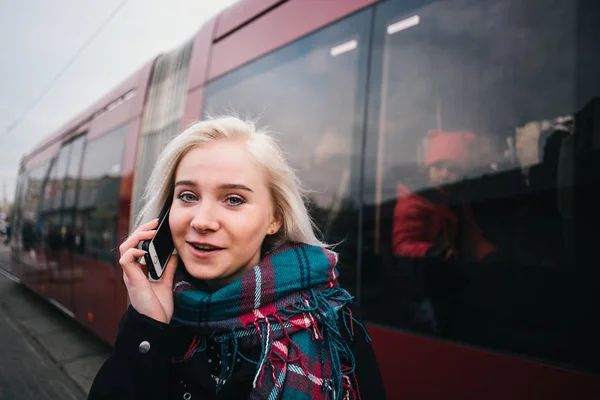 Οδός κομψό πορτρέτο του μια νεαρή και όμορφη γυναίκα που μιλούν από το τηλέφωνο σε φόντο κόκκινο τρένο. Το κορίτσι στο φόντο των δημόσιων μεταφορών. — Φωτογραφία Αρχείου