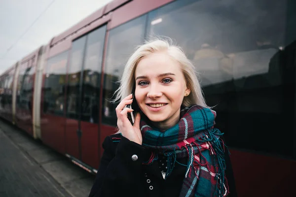 Νεαρός χαμογελαστό όμορφη γυναίκα μιλάμε στο τηλέφωνο για το φόντο της σύγχρονης αμαξοστοιχίας. Κορίτσι στέκεται στο σταθμό πλατφόρμα και χρησιμοποιεί το τηλέφωνο — Φωτογραφία Αρχείου