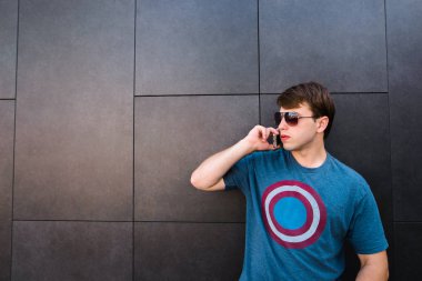 Bir cep telefonu üzerinde konuşurken ve yan yana gri bir duvara bakarak gözlüklü genç adam