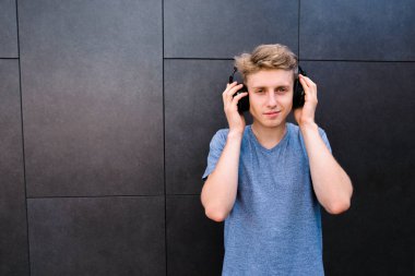Gözleri ile gülümseyen genç bir adam onun kulaklık arka plan gri bir duvar üzerinde müzik kapalı. Genç müzik dinlerken keyif alıyor
