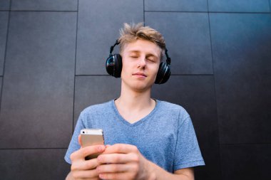 Genç, yakışıklı adam müzik onun Kulaklığımda gözleri kapalı dinliyor ve o gri bir duvar arka planda elini tutar.