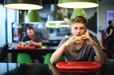 güzel genç öğrenci bir fast food Restoran bir hamburger yiyor. Lezzetli ve zararlı gıda. Nooning.