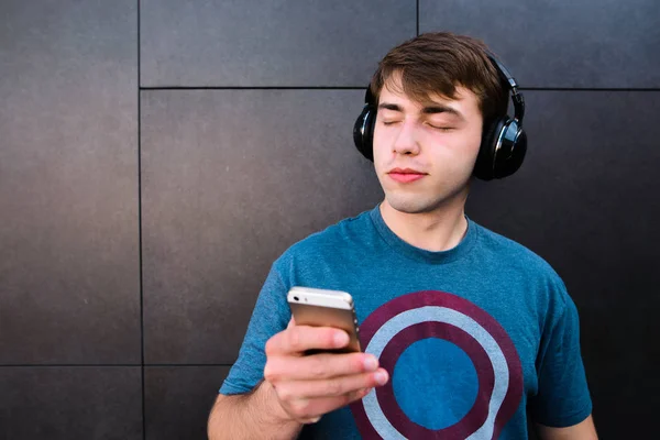 Мужчина с закрытыми глазами, и телефон в его руках, наслаждается музыкой в беспроводных наушниках на фоне стены . — стоковое фото