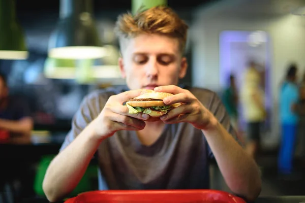 O delicioso hambúrguer nas mãos de um jovem estudante . — Fotografia de Stock