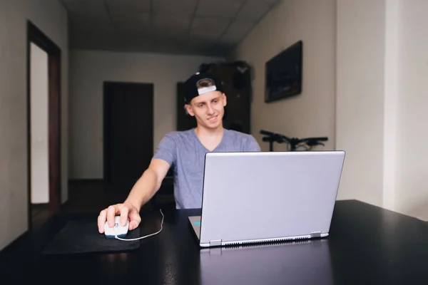 Un joven está sentado en casa por un portátil. Concéntrate en el portátil . — Foto de Stock